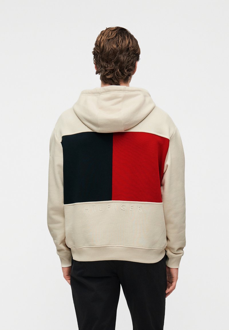 Φούτερ με κουκούλα σε ανοιχτό μπεζ χρώμα με αντίθετο σχέδιο μπλοκ σε ναυτικό μπλε και κόκκινο. Διαθέτει κεντημένο κείμενο "HILFIGER" κατά μήκος του τελειώματος.