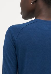 Long-sleeve blue ribbed shirt showcasing a round neckline and raglan sleeves, made of soft fabric with a subtle texture.