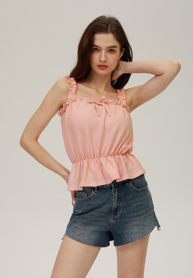 Top peplum cu textură de piersică, cu bretele volanate, detaliu cu fundă în față, asortat cu pantaloni scurți din denim închis, cu margine desfăcută.