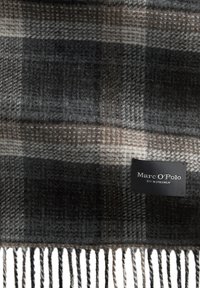 Grijs-bruin geruite sjaal van zacht wol, met franjes aan de randen en een zwart label met de tekst "Marc O'Polo, Est. in Stockholm."