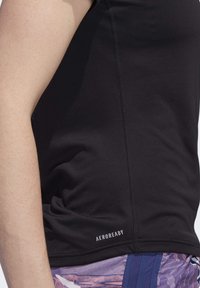 Vue de profil d'une personne portant un haut AEROREADY noir sans manches et un short de sport violet à motifs.