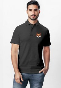 Dunkelgraues Poloshirt mit klassischem Kragen, ausgestattet mit einem orange-weißen Fuchs-Logo auf der linken Brust. Kurzarm, aus Baumwolle.