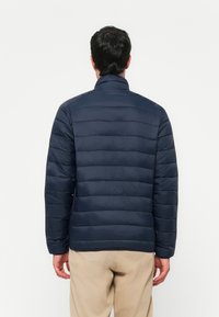 Mørkeblå pufferjakke med vandret quiltet design, høj krave og elastiske manchetter, lavet af let materiale for varme.