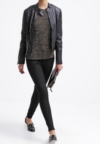 Svart läderjacka med en åtsittande design, texturerade ärmar, i kombination med en flerfärgad stickad tröja, svarta tajta jeans och blanka svarta ballerinas.