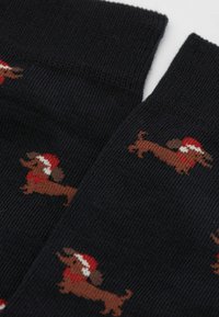 Czarne skarpetki z powtarzającym się wzorem brązowych jamników w czerwonych czapkach Mikołaja i szalikach.