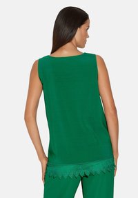 Grünes ärmelloses Oberteil mit einem geraden Rückendesign und einem Spitzenbesatz am Saum, der für eine strukturierte Detailgestaltung am unteren Rand sorgt.