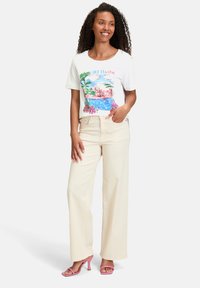 Hvid kortærmet t-shirt med en farverig strandgrafik. Kombineret med højtaljede, vide beige bukser og rosa hæle.