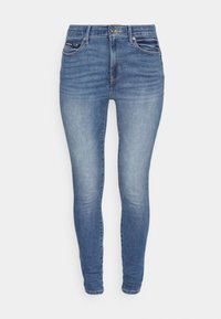 Jeans ajustados de denim; color azul medio con ligero desvanecimiento. Presentan un diseño estándar de cinco bolsillos y costuras en contraste.