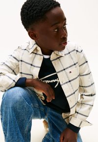 Rutet skjorte i creme med marineblå og grå striber, parret med en marineblå sweatshirts med hvid tekst, og blå denim jeans.