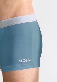 Boxer da uomo Sloggi in un morbido tessuto blu. Presenta un elastico in vita grigio chiaro e un logo bianco sul lato sinistro in basso.