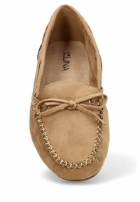 Zapato mocasín de gamuza color beige con punta redonda, lazo decorativo, costuras en la parte frontal y un forro interior suave.