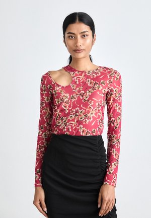 Long-sleeve top in pink floral pattern, featuring an elongated cutout at shoulder. Material is lightweight and sheer. Black ruched skirt below.