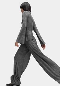 Metallisch zilveren top met uitlopende mouwen gecombineerd met een broek met wijde pijpen, beide met een gestructureerde afwerking. De outfit heeft een strakke silhouet.
