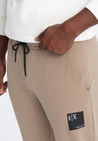 Beiga joggers i mjukt tyg, med en svart dragsko, sidofickor och en logotypapplikation på låret.