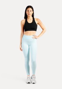 Svart sport-bh för träning kombinerad med ljusblå höga leggings. Matchas med grå sneakers. Enkel, figurnära design med slät textur.