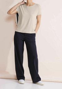 Beige t-shirt med kort ärm i kombination med lösa marinblå byxor. Outfiten har en avslappnad passform och mjukt tyg, lämplig för vardagsbruk.