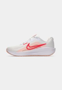 Zapatilla de correr Nike con una parte superior de malla blanca y rosa, un prominente swoosh rojo y una suela exterior suave y texturizada con un acento en rosa claro.