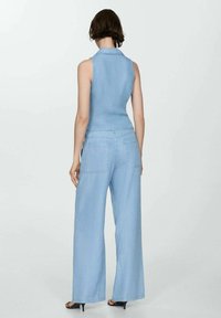 Ljusblå denimsammanställning med ärmlös design, vida byxor och bakfickor. Mjuk textur och krage detalj synlig.