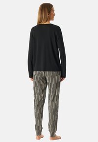 Zwart longsleeve shirt gecombineerd met gestreepte, taps toelopende pyjamabroek met verticale lijnen in zwart en crème. Zachte stof, ontspannen pasvorm.