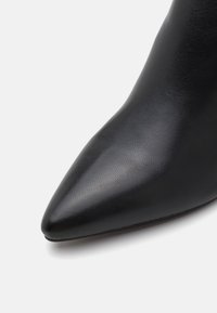 Black pointed toe boot made of textured leather, featuring a sleek silhouette and smooth finish, with a thin sole.