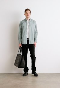 Lichtgroen overhem shirt over een wit T-shirt, zwarte broek, zwarte schoenen en een zwarte tote bag met ingedrukte tekst. Minimalistisch ontwerp.