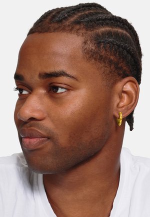 Boucle d'oreille en or sur l'oreille d'une personne, en forme ronde, finition brillante, surface texturée, portée avec une chemise blanche, vue de profil en gros plan.