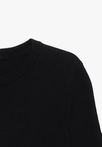 Mustan villapaidan, jossa on pyöreä kaula-aukko ja ribattu kaulus. Kangas näyttää pehmeältä, sillä on sileä pinta ja minimaalinen yksityiskohtaisuus.