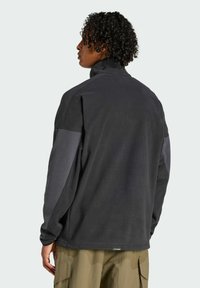 Pull-over en molleton gris foncé avec des accents gris clair sur les épaules. Design à col montant, tissu texturé, coupe décontractée, coutures plates et étiquette visible à l'ourlet.
