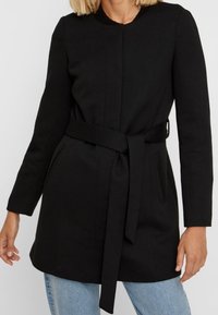 Black belted coat with a straight cut, long sleeves, side pockets, and textured collar. Fabric appears smooth and warm.