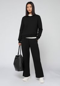 Zwart sweatshirt en broek outfit met een relaxte pasvorm. Vergezeld van een zwarte leren tote bag en witte sneakers, met een eenvoudige uitstraling.