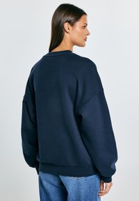 Námořnická oversized mikina z měkké látky s kulatým výstřihem a spadlými rameny. Má žebrované manžety a lem, ležérní design.