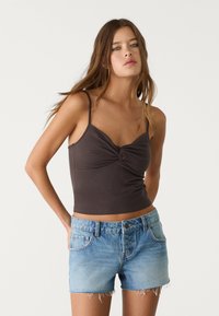 Top corto marrone scuro con design anteriore annodato, abbinato a pantaloni corti in denim blu chiaro con orlo sfrangiato e stile a cinque tasche.