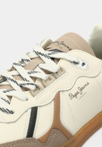 Bēšas un baltas sporta kurpes ar teksturētu ādu un zamšādas paneļiem, melniem akcentiem un baltām auklām, zīmola nosaukums "Pepe Jeans London".