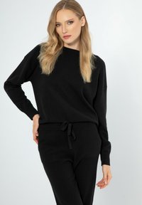 Schwarzes Strick-Loungewear-Set mit einem langärmeligen Oberteil mit Rundhalsausschnitt und Hosen mit Kordelzug an der Taille. Weiche Textur und lockere Passform.