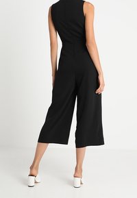 Czarny jumpsuit bez rękawów z wysoką szyją, szerokimi nogawkami i gładką strukturą. Prosty fason z ukrytym zamkiem z tyłu i bez wzorów.