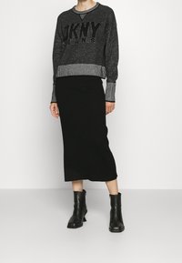 Svart ribbad kjol i kombination med en mörkgrå, texturerad tröja med en iögonfallande "DKNY" logotyp och randiga ärmslut. Svarta ankelstövlar fulländar looken.