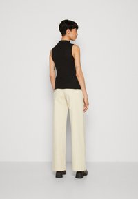 Must have kõrge kaelusega must ilma varrukateta top, millele on sobitatud lohakad heledad kreemivärvi püksid ja jämeda musta talla kingad, esitleb minimalistlikku disaini.