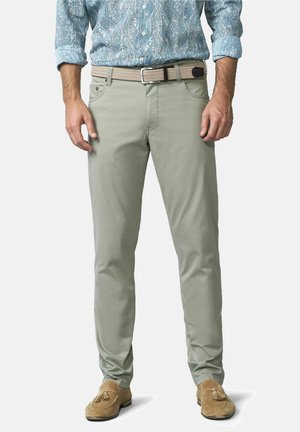 Man die lichtgroene slim-fit broek, beige gevlochten riem, blauw patroonhemd en tan suède loafers met kwastjes draagt, rechtopstaand.
