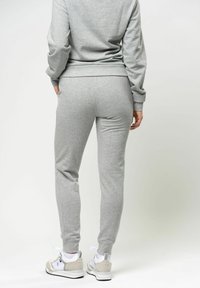 Grijze katoenen sweatshirt en joggers met ribbels aan de mouwen en taps toelopende pijpen, gecombineerd met witte sportschoenen met grijze accenten.