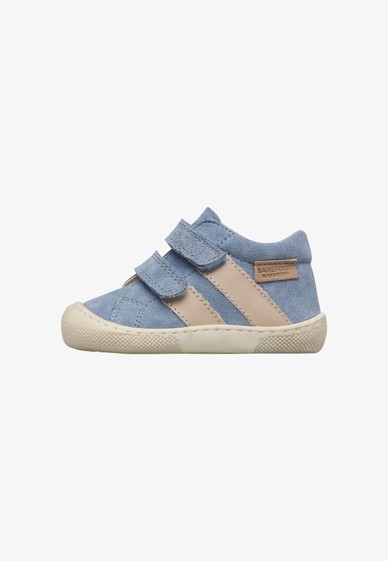 Zapatilla para niño pequeña de gamuza azul con rayas beige, dos correas de velcro y suela de goma texturizada, aislada sobre fondo blanco.