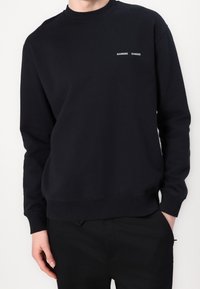 Sudadera negra de cuello redondo hecha de algodón, con logo bordado en el pecho, puños y dobladillo acanalados, y un corte holgado.