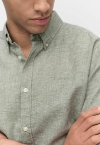 Lichtgroen, getextureerd overhemden met kraag. Bevat kleine knopen en een vaag logo dat op de stof is geborduurd.