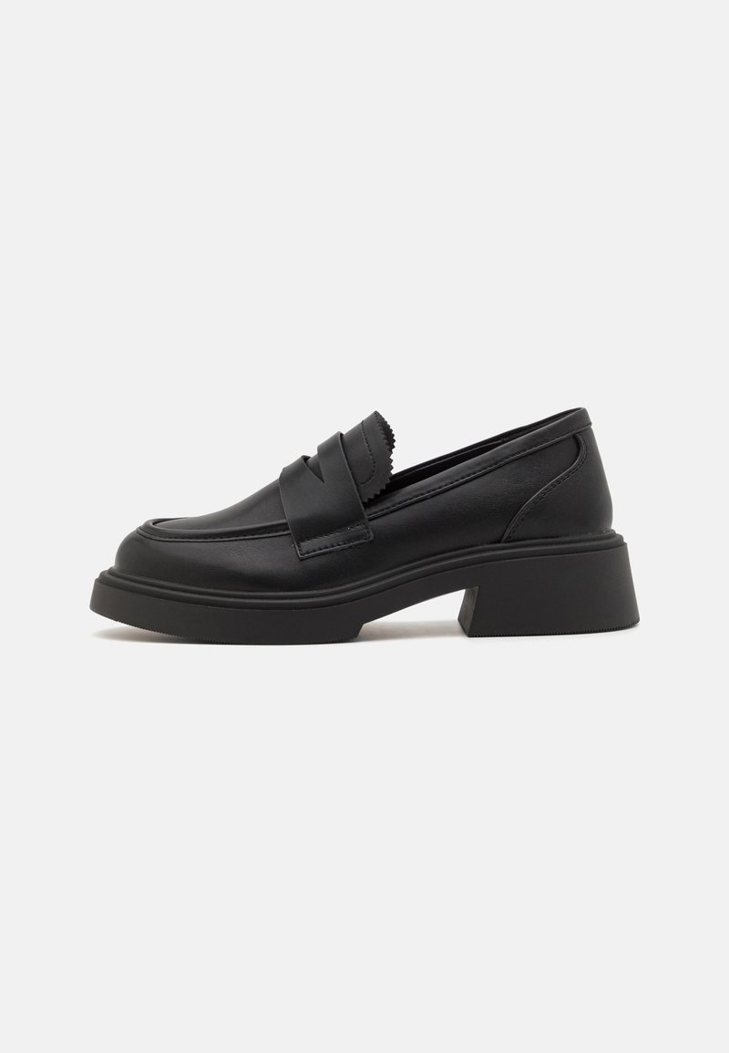 Mocassins noirs en cuir lisse, avec un talon épais, des accents festonnés sur le dessus et un design minimaliste.