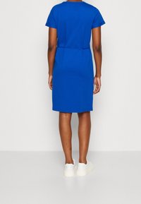 Robe en coton bleu à manches courtes avec une coupe décontractée, détail de taille cintrée et longueur au genou, associée à des baskets blanches.