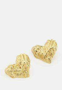 Guldörhängen i form av hjärtan med en texturerad, vågig design. Den polerade ytan förstärker reflektionerna och framhäver de intrikata detaljerna.