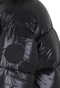 Giacca a vento nera con finitura lucida, design trapuntato e toppa rotonda con logo sulla parte superiore del braccio.