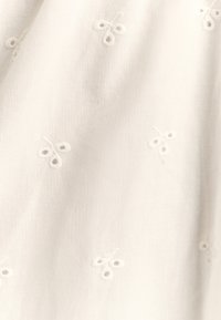 Weißer Stoff mit zarten gestickten Blumenmustern. Weiche Textur mit dezentem Glanz. Das Design umfasst kleine, runde Blumen.