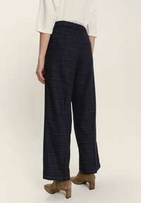 Marineblau gemusterte weit geschnittene Hose mit elastischem Taillenbund und geradem Schnitt. Das Material wirkt strukturiert mit feinen goldenen Linien durchzogen.