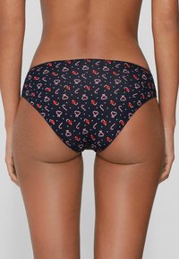 Dół od bikini w kolorze granatowym z powtarzającym się wzorem czerwonych kokardek i lasek cukrowych. Gładka tkanina o umiarkowanym wycięciu i bezszwowym kroju.