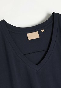 Granatowa koszulka V-neck wykonana z miękkiego materiału. Posiada skórzaną metkę z nazwą marki oraz przeszyty dekolt dla podkreślenia detali.